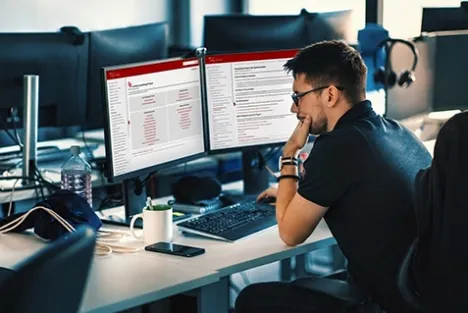 Man in glasses reading documentation on two monitors