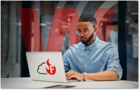 black man with a chinstrap beard and glasses working on a laptop with a red and black WatchGuard FireCloud icon on the back