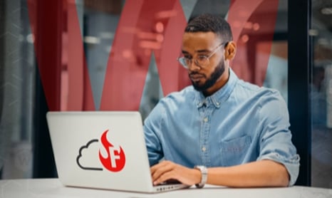 black man in glasses working at a laptop with a WatchGuard FireCloud sticker on the back