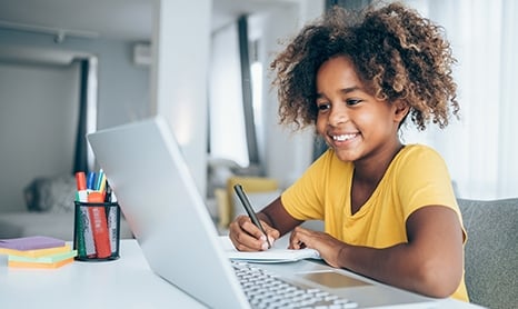 Young child smiling at a laptop computer and taking notes