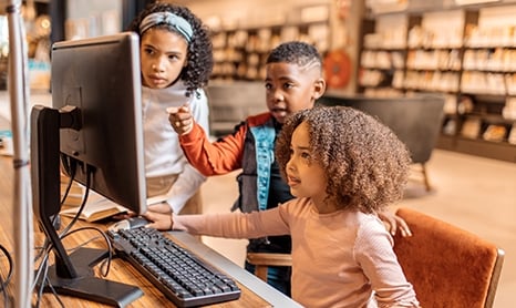 Young kids around a computer in a library