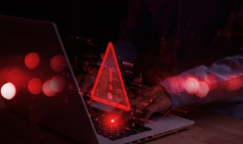  Cybersecurity warning symbol glowing red over a laptop keyboard, representing malware threats, malicious code, and cyberattack detection.