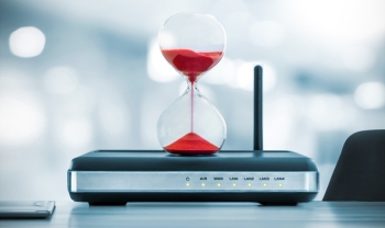 Hourglass sitting on a network router, symbolizing the shrinking time cybersecurity teams have to patch vulnerabilities before attackers exploit them.