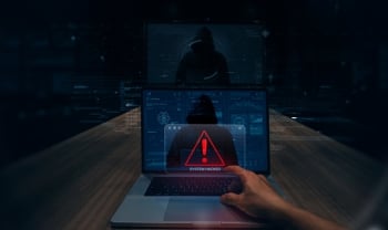 Dark cybersecurity illustration showing a hooded hacker on a laptop screen with a red security warning symbol, representing AI security vulnerabilities, hidden cyber threats, and potential data breaches.