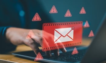 Person using a laptop with a warning overlay showing a suspicious email icon, representing a phishing or malware attack.