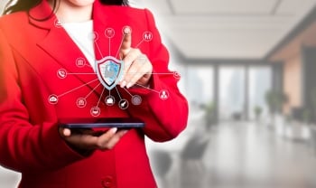 Business professional using a tablet with a digital cybersecurity shield and connected security icons overlayed on screen.