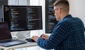 Developer working at a multi-monitor coding workstation with software code displayed across screens in a modern office environment.