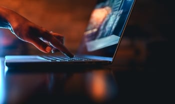 Person using a laptop in a dark setting, representing digital identity, AI access, and cybersecurity risk.