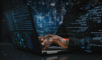 Person using a laptop surrounded by overlaid computer code, representing AI-powered cyberattacks, hacking, and cybersecurity threats.