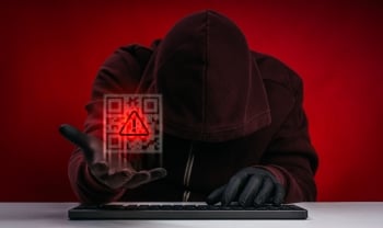 Hooded cybercriminal holding a glowing QR code with a warning symbol, representing QR code phishing, social engineering, and cryptocurrency cyber threats.