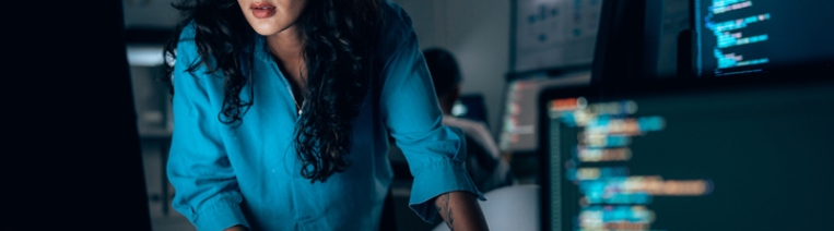 Cybersecurity professional analyzing code on multiple monitors in a modern security operations center, investigating threats and system defenses.