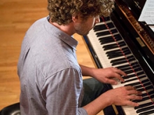 Man with curly brown hair playing the piano