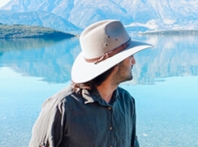 Man in a hat standing in front of mountains and a lake