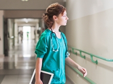 Woman in green scrubs with a stethoscope around her neck carrying an iPad