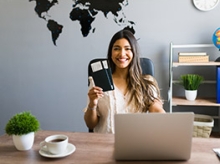 Smiling woman in a home office holding her wallet up in front of an open laptop