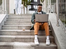 Young black man sitting on university steps working on a laptop