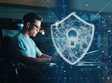 Man in glasses working at a computer with a shield icon made of lights in front