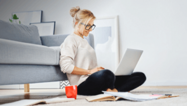 Woman sitting in front of her couch working on a laptop