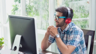 Man in headphones sitting a a desk looking at a monitor