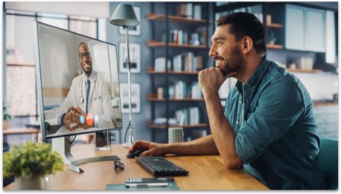 Man in a blue shirt at home talking to a doctor on his computer monitor