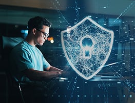 Man in glasses working at a computer with a shield icon made of lights in front