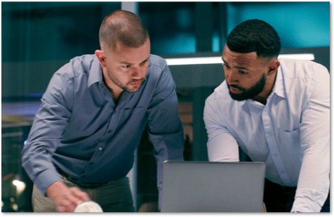 Two men leaning over a laptop, looking at the screen